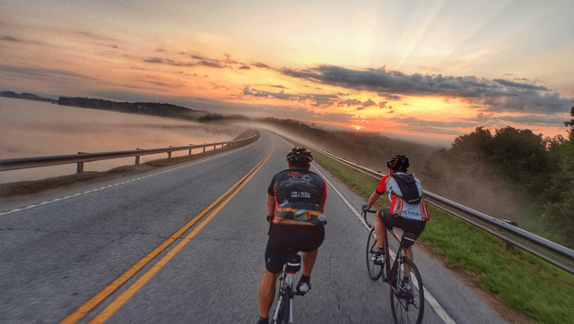 Two people riding bikes on a road at sunset.