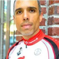 A man in red and white shirt standing next to brick wall.