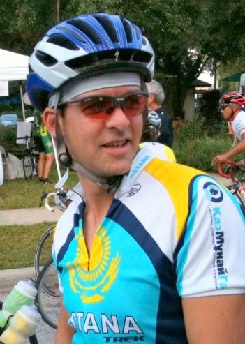 A man in blue shirt and helmet standing next to bicycle.